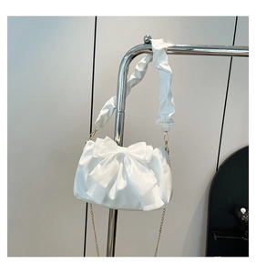 Macro detail of white bow handbag showing satin leather texture and gold chain strap