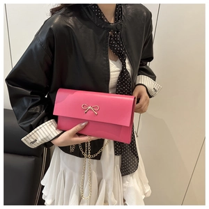 Detail of a bright pink crossbody bag with a gold metal bow and delicate chain strap