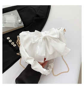 Detail view of white shoulder bag with large bow design and gold chain strap