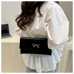 Side view of black envelope chain bag with golden bow worn on shoulder by a model
