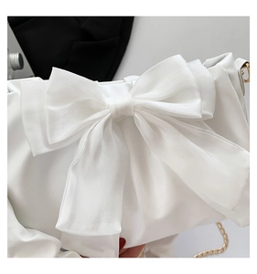 Detail of a white glossy shoulder bag with a large tulle bow and gold chain strap