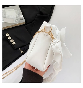 Detail view of white shoulder bag featuring wide pleated bow design and golden chain strap