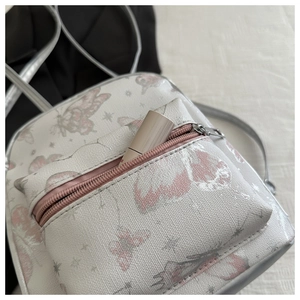 Close-up of white backpack featuring pink butterfly prints and silver zipper pocket detail