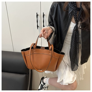 Detail view of caramel brown leather tote bag showing white stitching and shoulder straps