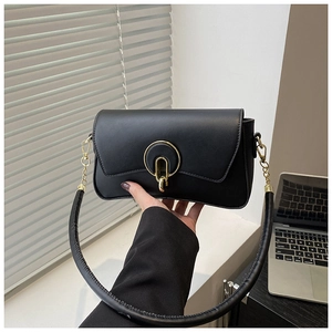Close-up of a matte black handbag with a circular gold buckle and thick shoulder strap