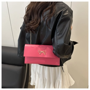 Hot pink envelope clutch with gold bow detail and chain strap worn over a white skirt