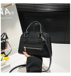 Detail of black pebbled leather handbag with gold zippers and detachable strap