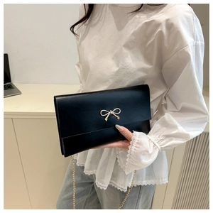Detail of black matte leather crossbody bag featuring a delicate gold bow metal buckle