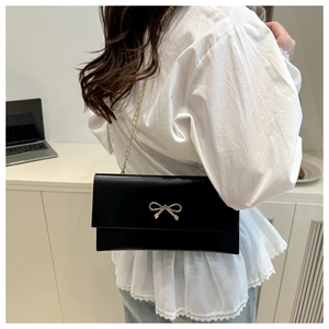 Crossbody view of a black leather square bag with golden bow buckle and chain strap