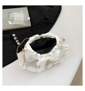 Detail of white pleated shoulder bag featuring a large bow and elegant gold chain strap