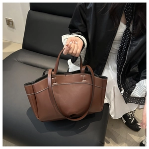 Detail of a large brown tote bag with white contrast stitching and double handle straps