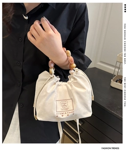 Détail d'un sac crème avec poignée en perles acryliques colorées et logo ours brodé