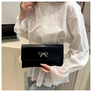 Detail of elegant black crossbody bag with gold bow clasp and sleek chain strap