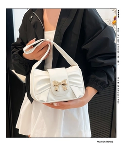 Detail of white leather shoulder bag featuring a gold bow buckle and pleated texture