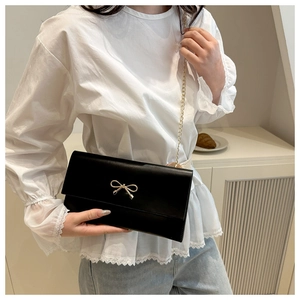 Detail of black crossbody bag with gold bow clasp and metal chain on a model