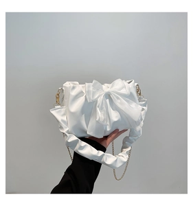 Detail of white pleated handbag featuring a large organza bow and elegant gold chain strap