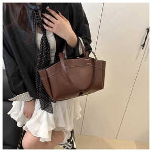 Brown leather tote bag with white contrast stitching detail shown on a model