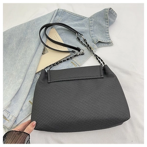 Detailed view of black geometric textured tote bag with silver chain strap on white fabric