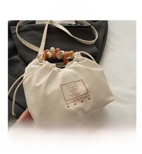 Sac en satin beige à cordon avec poignée en perles ambre et détail de logo d'ours