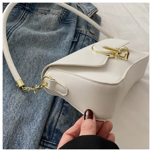Détail du sac à bandoulière blanc avec boucle dorée sur une veste en jean