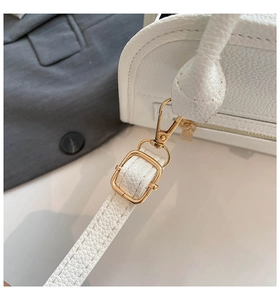 Detail of white lychee leather texture and golden metal hardware on a Boston bag
