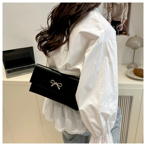 Detail of black crossbody bag featuring a decorative golden bow and elegant metal chain strap