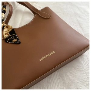 Gros plan d'un cabas en cuir mat marron avec surpiqûres blanches et détail foulard soie