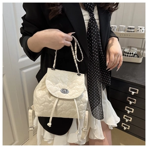Detail of white heart-quilted leather backpack with silver turn-lock and chain strap