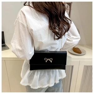 Detail of a black PU leather crossbody bag with a gold bow and slim chain strap