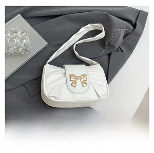Detail of white pleated shoulder bag with golden bow buckle on dark blazer background