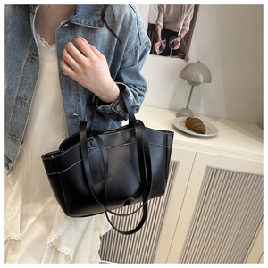 Detail of a black tote bag with white contrast stitching on minimalist leather surface