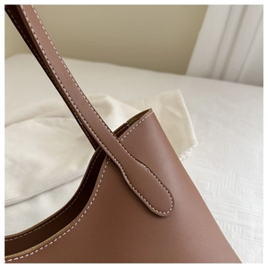Détail du sac cabas en cuir marron montrant les surpiqûres blanches et l'attache de bandoulière