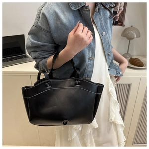 Detail of black leather tote bag with white contrast stitching and dual handles