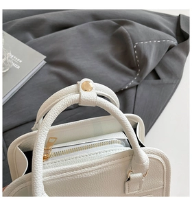 Detail shot of white litchi grain leather Boston bag with light gold metal zippers