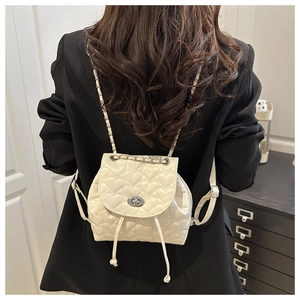 Detail of white heart quilted backpack featuring gold chain straps and drawstring closure