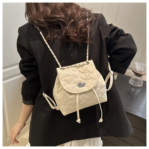 Detail of cream white heart-quilted backpack with metal twist lock and chain straps