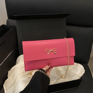 Elegant rose pink crossbody bag with gold bow clasp and metal chain on silk cloth