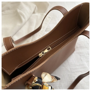 Détail du sac fourre-tout en cuir caramel avec fermeture éclair dorée et foulard en soie