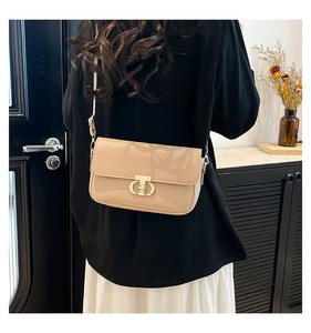 Detail of beige leather crossbody bag featuring a golden circular clasp on a model