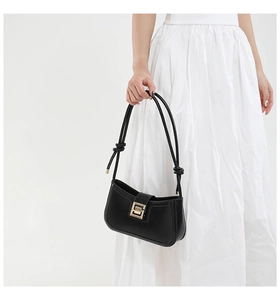 Detail of black leather shoulder bag with gold square buckle and knotted strap accents