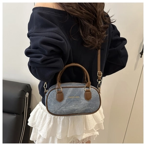 Détail du sac bandoulière vintage en denim avec anses en cuir brun et texte doré mode