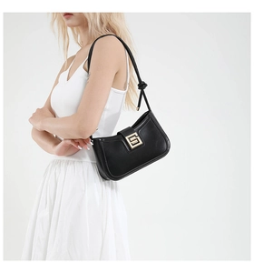 Detail of a black minimalist leather baguette bag featuring a metal buckle and knot strap