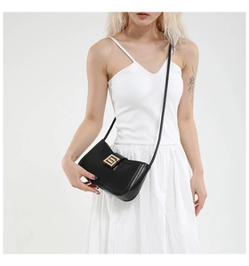 Detail of minimalist black leather crossbody bag with elegant gold metal buckle accent