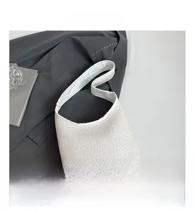 Detailed view of white woven shoulder bag with wide strap on grey textured background
