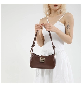 Detail of dark brown leather handbag featuring unique knotted strap and gold geometric buckle