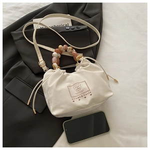 Detail of cream drawstring cloud bag with colorful resin bead handle and bear logo