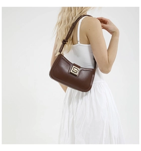 Detail view of deep brown leather baguette bag with a gold square clasp on white