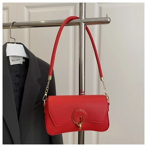 Détail du sac bandoulière en cuir rouge avec boucle métallique ronde et chaîne dorée
