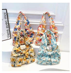 Detail of four floral fabric shoulder bags with large bow accents on a white display stand