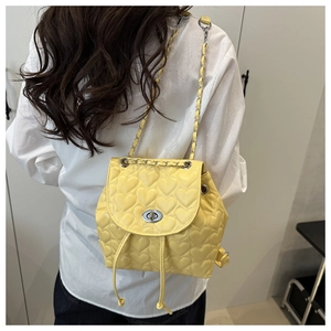 Detail of yellow heart-quilted backpack with silver chain strap worn by a model